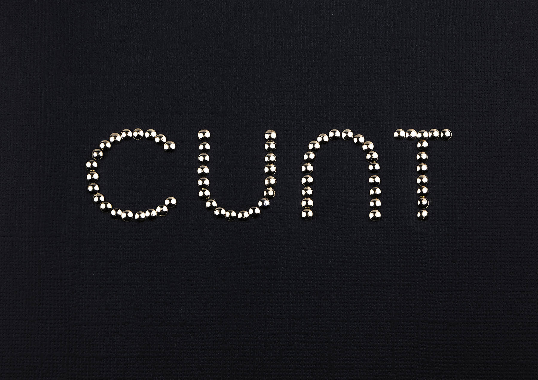 Brass studs spell cunt on black card