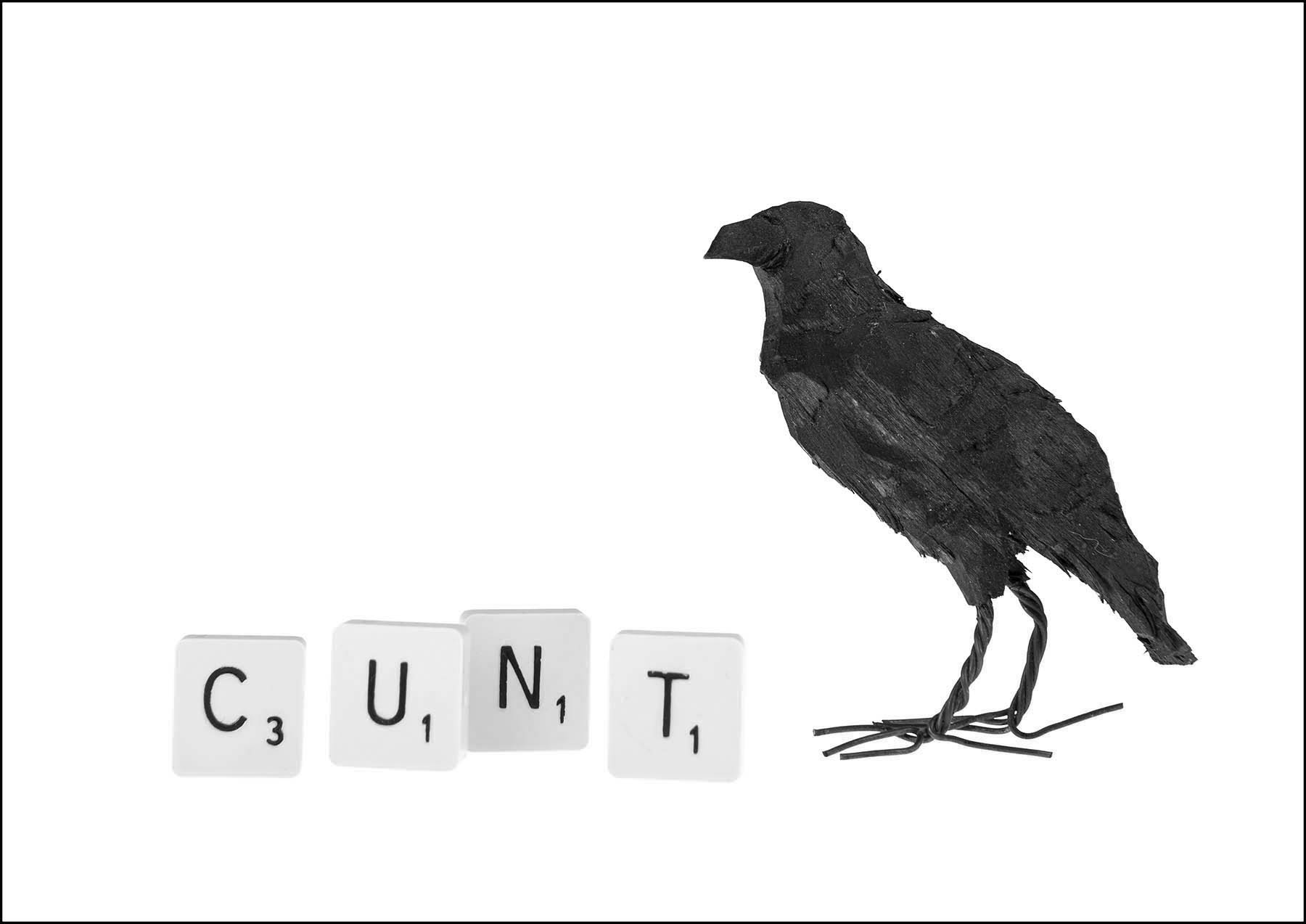 Scrabble tiles spell cunt next to a carved wooden raven 